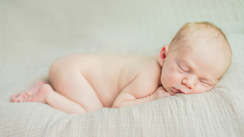 Nacktes Baby schläft in Kuschelstellung bäuschlings auf hellem Stofftuch